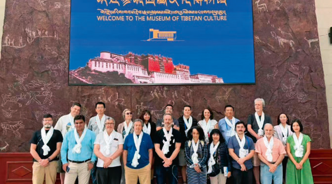 Grupo de visitantes posa bajo un cartel de bienvenida al Museo de Cultura Tibetana.