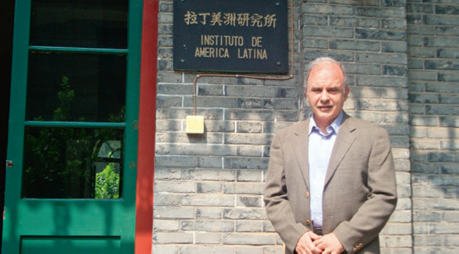 Néstor Restivo junto a una placa del Instituto de América Latina, frente a una fachada de ladrillos.