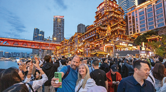 Turistas recorren una zona tradicional iluminada entre edificios modernos de Chongqing