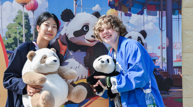 Dos visitantes posan con peluches de panda frente a una ilustración de pandas.